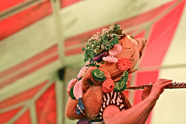 Person in a flowery costume plays a flute
                        facing away from the camera