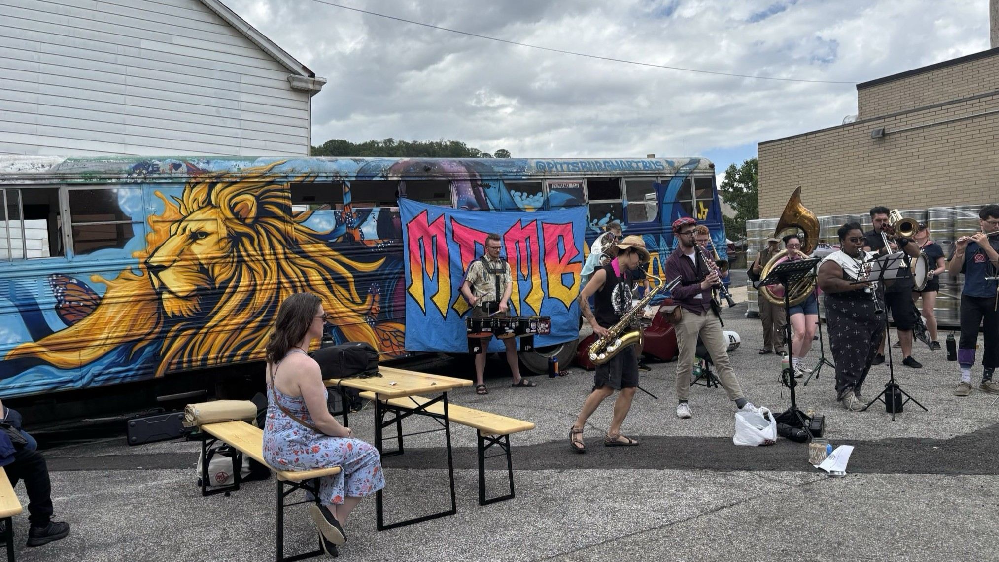 Band performs in front of a bus painted with
                        a stylized graphic of a lion while 
                        spectators sit at picnic tables nearby